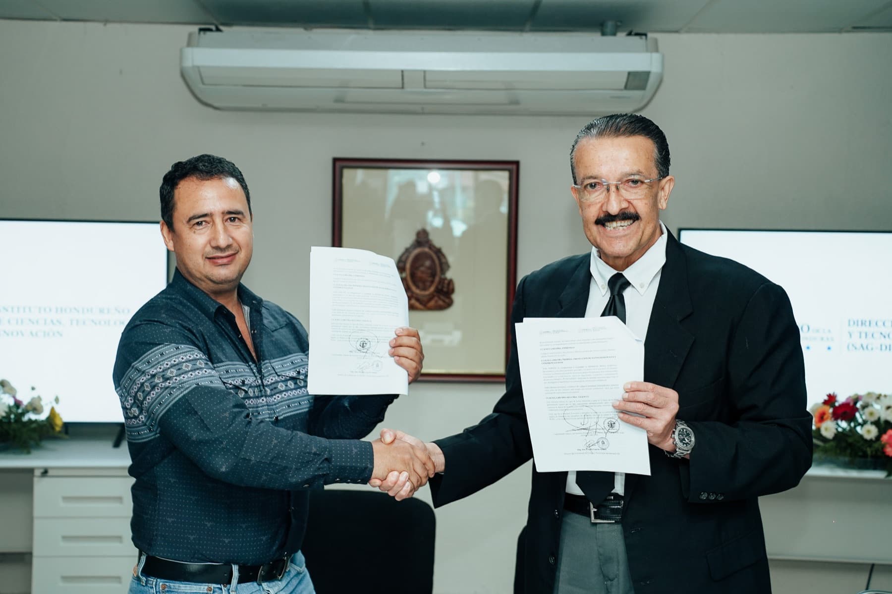 Autoridades de DICTA e IHCIETI estrechan sus manos y muestran el convenio firmado
